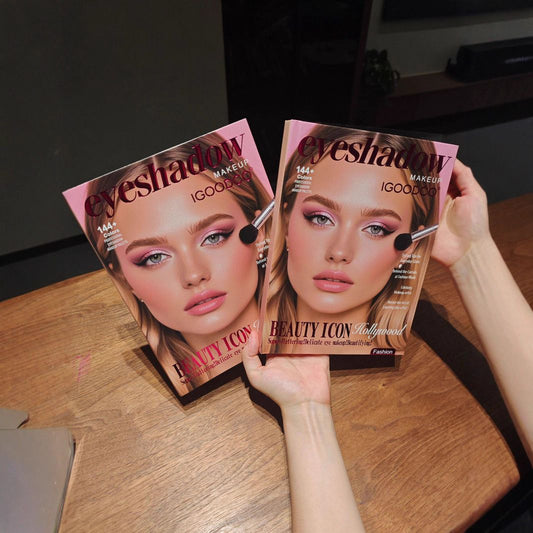 Two copies of Eyeshadow Magazine (Issue 164) held up by hands over a wooden table. The covers feature a model with pink eyeshadow and makeup, with the title 'eyeshadow' in a stylized font.