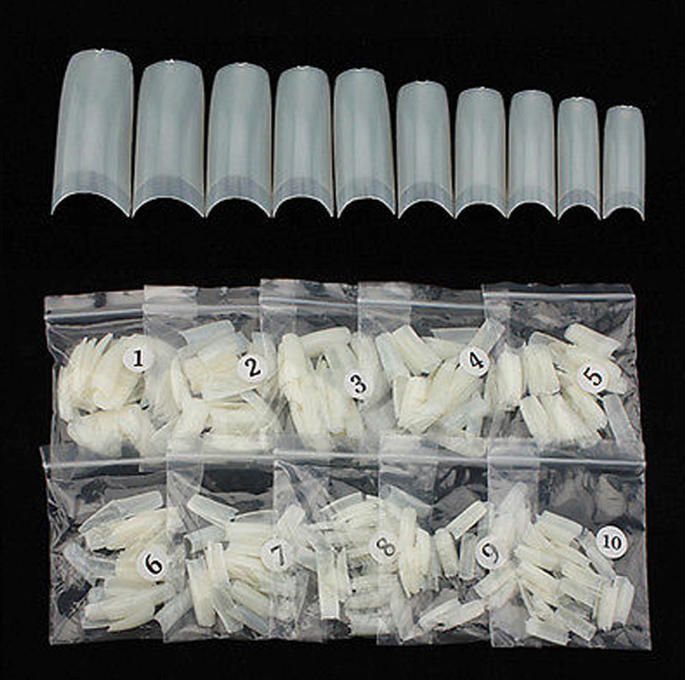 A set of 15 clear plastic nail tips arranged in a row above 10 numbered clear plastic bags containing white nail wraps, all photographed against a solid black background.