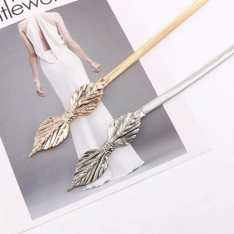 Two decorative hair sticks with leaf-shaped metal ends, one in gold-tone and one in silver-tone, displayed on a white surface with a fashion magazine page underneath.