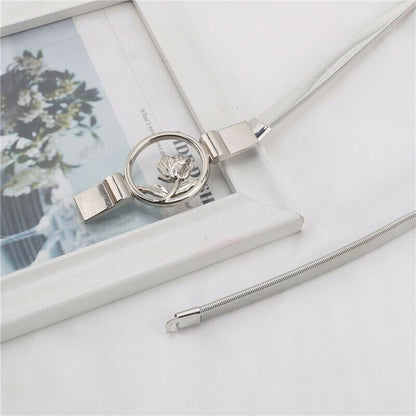 A silver-toned snake chain necklace with a circular pendant featuring a rose design, displayed on a white surface next to a white picture frame.