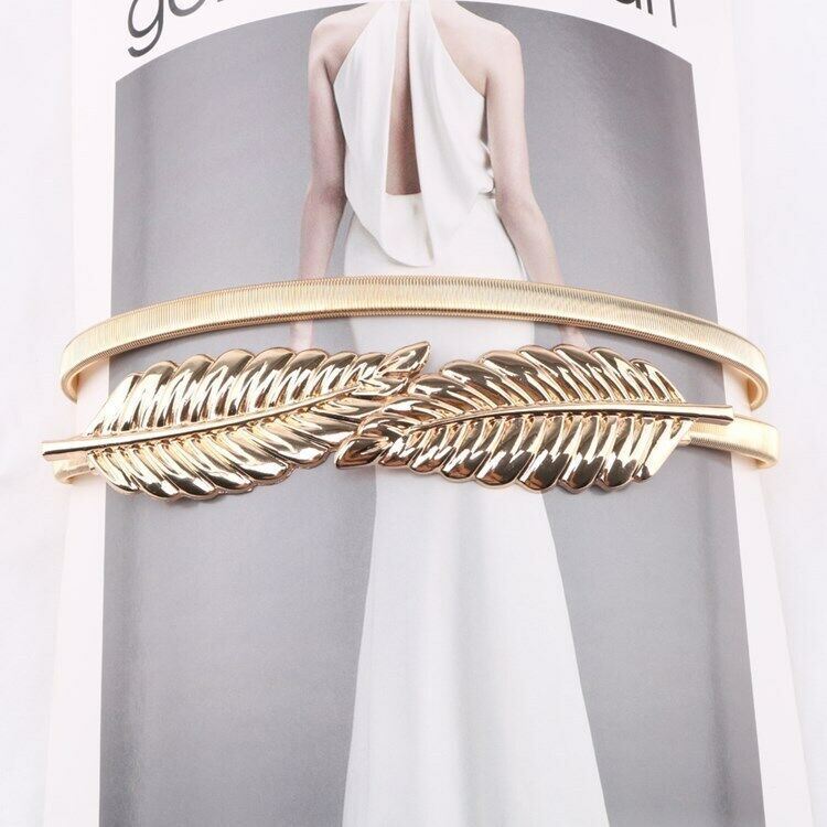 A gold-toned metal cuff bracelet featuring a large feather motif across the front, displayed against a magazine-style background with a model in a white dress.
