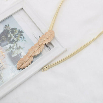 A gold-toned metal collar with a layered feather-shaped centerpiece, styled on a white fabric surface next to a white picture frame.