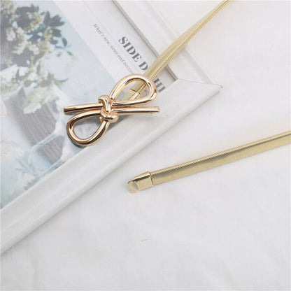 A gold-toned metal accessory with a bow-shaped end and a coiled snake-like band, photographed on a white surface with a magazine underneath.