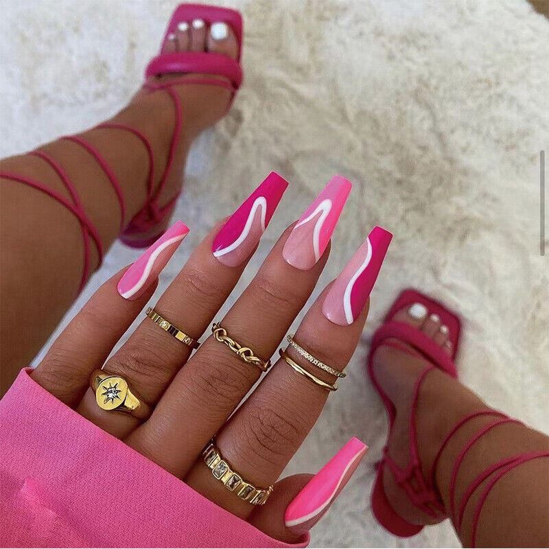 Close-up of a hand with pink nail polish and multiple gold rings, wearing pink strappy sandals on a light background.