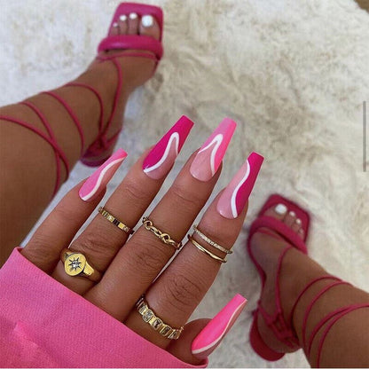 Close-up of a hand with pink nail polish and multiple gold rings, wearing pink strappy sandals on a light background.