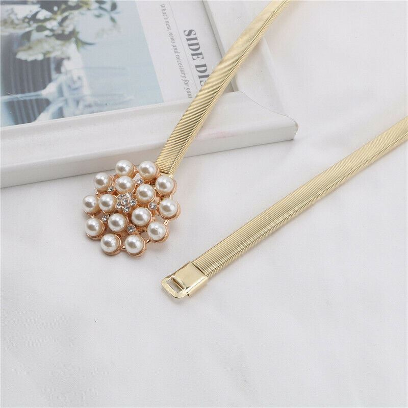 A gold-tone snake-skin style hair stick with a flower-shaped pearl cluster and a central clear rhinestone, displayed on a white fabric surface next to a white book.