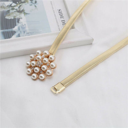 A gold-tone snake-skin style hair stick with a flower-shaped pearl cluster and a central clear rhinestone, displayed on a white fabric surface next to a white book.