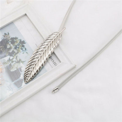 A silver-toned feather pendant necklace with a matching chain, styled on a white surface next to a white picture frame.