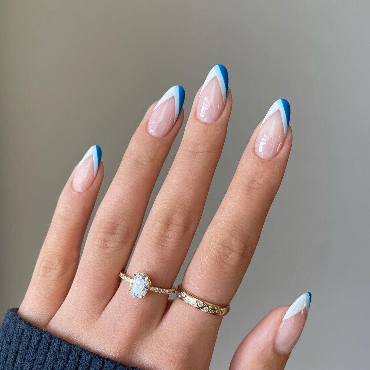 Hand with blue and white nail design wearing two rings on a neutral background