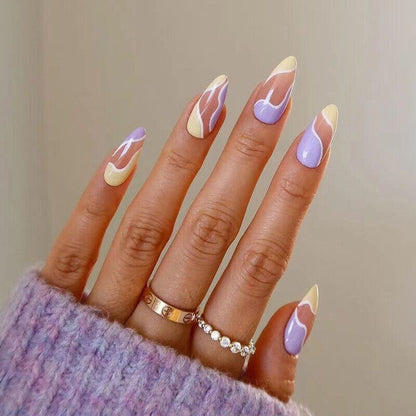 A close-up of a hand with long almond-shaped nails painted in a pastel French manicure style with lavender, cream, and white swirls. The hand is wearing a lavender knit sweater and two rings, against a soft neutral background.