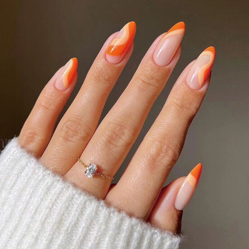 Hand with orange and beige nail polish wearing a white sweater and ring on a neutral background