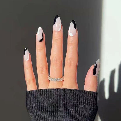Hand with black and white nail design wearing a black sleeve against a gray background