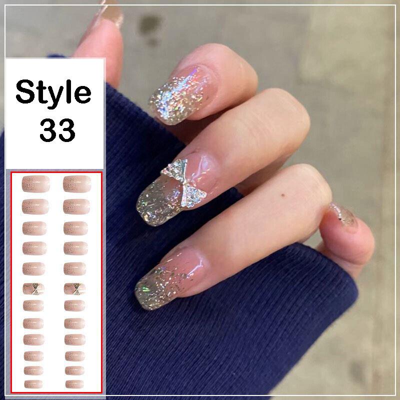 A hand wearing press-on nails in style 33, showing a glossy nude-pink base with silver glitter and a small rhinestone bow accent on one nail. An inset on the left shows the sheet of false nails and style number 33.