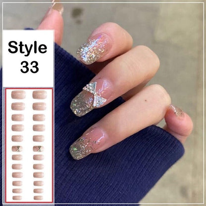 A hand wearing press-on nails in style 33, showing a glossy nude-pink base with silver glitter and a small rhinestone bow accent on one nail. An inset on the left shows the sheet of false nails and style number 33.