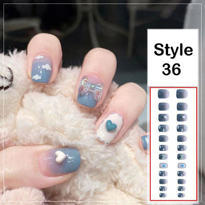 A hand with decorated fingernails in a blue and white style, resting on a white fluffy surface, next to a product sheet labeled 'Style 36' showing the nail wrap designs.