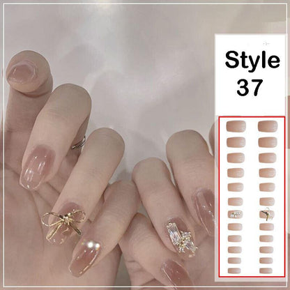 A close-up of manicured hands wearing glossy nude-pink press-on nails, with two decorative accent nails featuring gold bow and crystal details. A white panel on the right shows nail style number 37 with multiple nude-pink nail color options outlined in red.