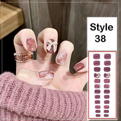 A hand wearing press-on nails in a coordinated set, with one nail decorated in white and a small bow motif. The nails have a glossy mauve-pink base with subtle glitter or marble effects.