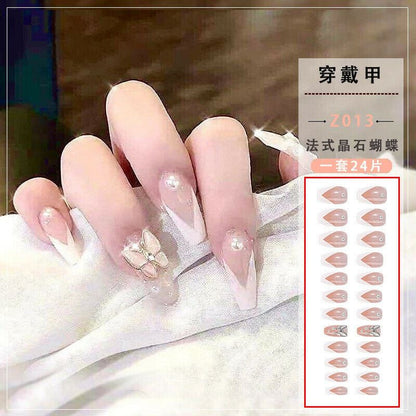 A hand displaying long almond-shaped press-on nails with French tips, pearl accents, and a butterfly design, alongside a product sheet showing 24 different nail color and shape options.