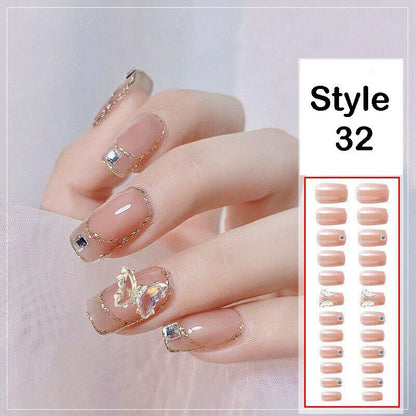 A hand displaying a set of natural nail wraps in a nude pink color with gold glitter borders and decorative rhinestone accents, alongside a white panel labeled 'Style 32' showing the total number of nail stickers included.