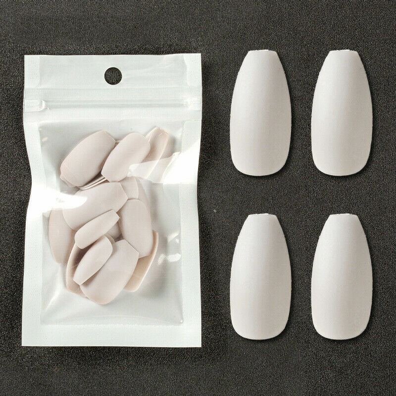 Four white false nail tips displayed next to a clear plastic pouch containing additional matching nail tips, set against a dark textured background.