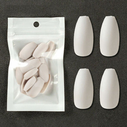 Four white false nail tips displayed next to a clear plastic pouch containing additional matching nail tips, set against a dark textured background.