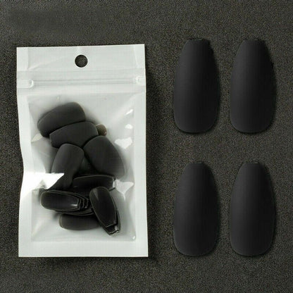 Four matte black coffin-shaped press-on nails displayed next to their clear plastic resealable pouch on a dark textured background.