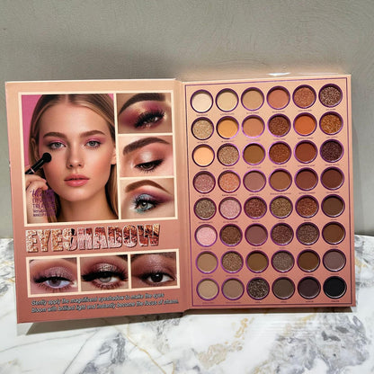 An open eyeshadow palette displayed on a marble surface against a gray wall. The left page shows a model wearing the eyeshadow makeup with before-and-after eye makeup panels and the text 'EYESHADOW'.