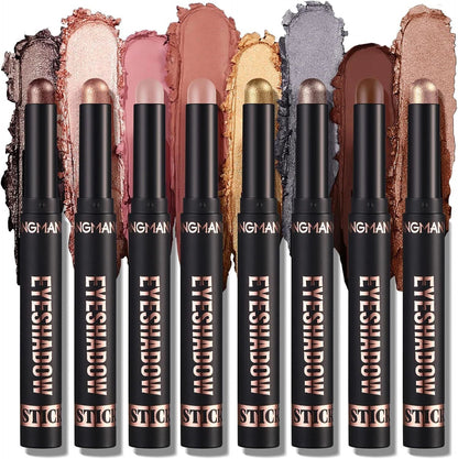 Eight eyeshadow stick pencils in assorted shades are lined up vertically, each with a textured eyeshadow swatch behind it. The black tubes have rose gold lettering that reads 'EYESHADOW STICK'.