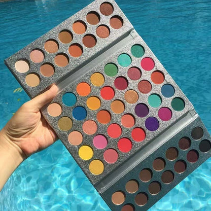 Makeup palette with a variety of colors held by a hand against a blue water background