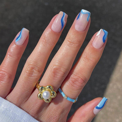 Hand with blue and white nail design wearing a gold ring and blue band on a dark background