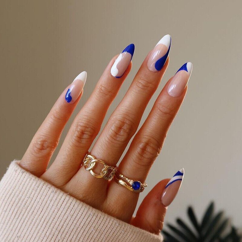 Hand with blue and white nail design wearing gold rings on a neutral background