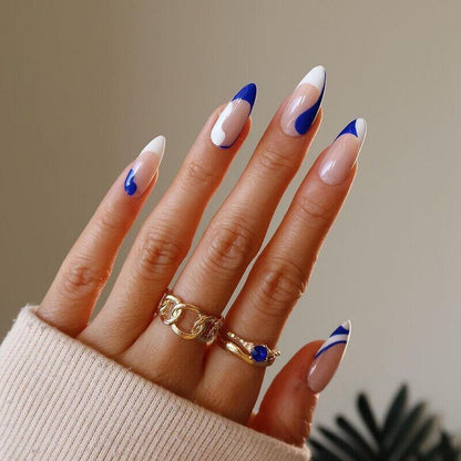 Hand with blue and white nail design wearing gold rings on a neutral background