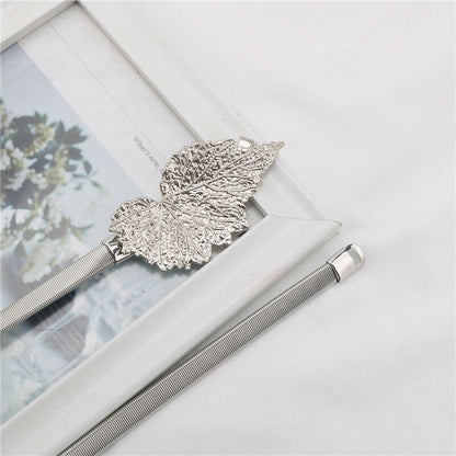 A silver metal mesh pen with a decorative leaf-shaped clip, resting on a white picture frame against a white fabric background.