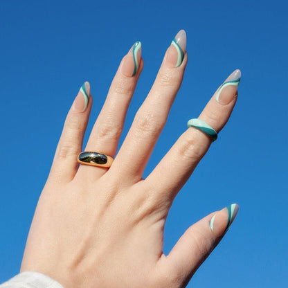 Hand with green and white striped nail polish against a clear blue sky