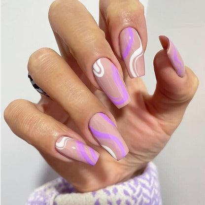 A close-up of a hand showcasing coffin-shaped nails with a glossy nude pink base and purple and white wavy patterns.