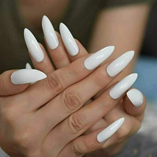 A close-up of a hand with long, glossy white stiletto-shaped press-on nails or a white manicure, shown against a softly blurred background.