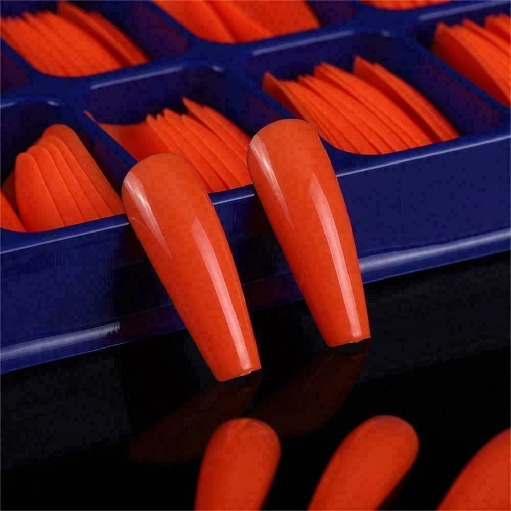 Close-up of orange nail tips in a blue organizer on a reflective surface.