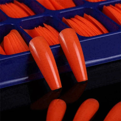 Close-up of orange nail tips in a blue organizer on a reflective surface.
