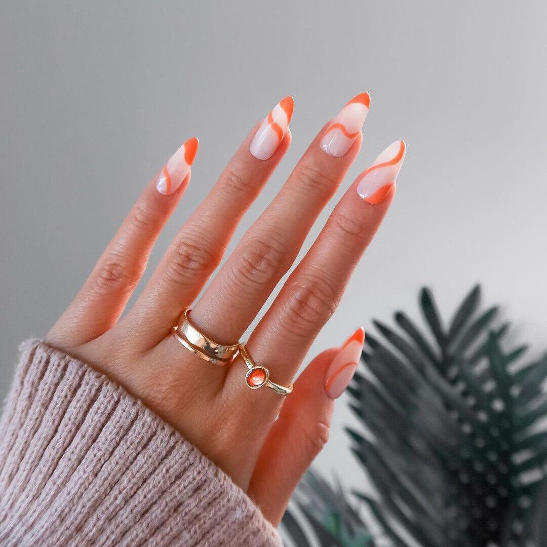 Hand with orange and white nail polish wearing a gold ring against a gray background