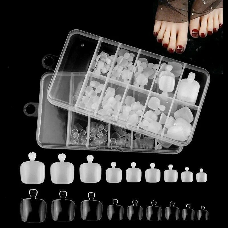 A clear plastic compartment organizer filled with white press-on nail tips and small clear rhinestones, shown on a black background with a pair of feet at the top and a row of black press-on nail tips at the bottom.