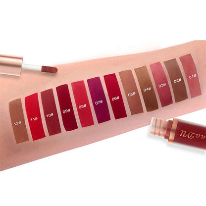 A lip gloss color swatch chart showing 15 different shades from beige to deep burgundy, displayed on a model's forearm with two tubes of gloss partially visible.
